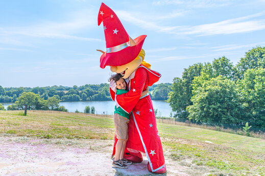 Lachend kind knuffelt campingmascotte tijdens animatie op camping CAPFUN Lac de Ribou in Cholet (49).