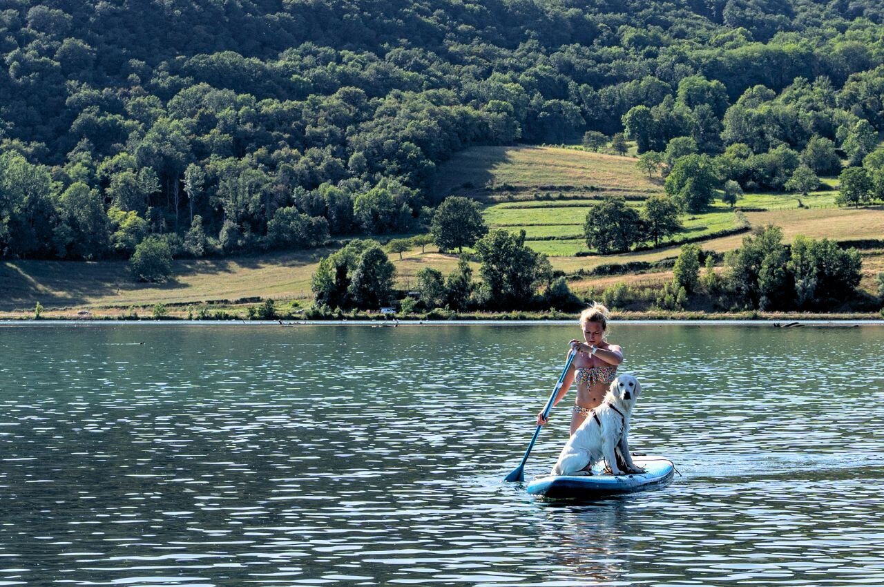 Vrouw en hond op paddleboard, meer. Op camping CLICOCHIC Lac du Lit du Roi.