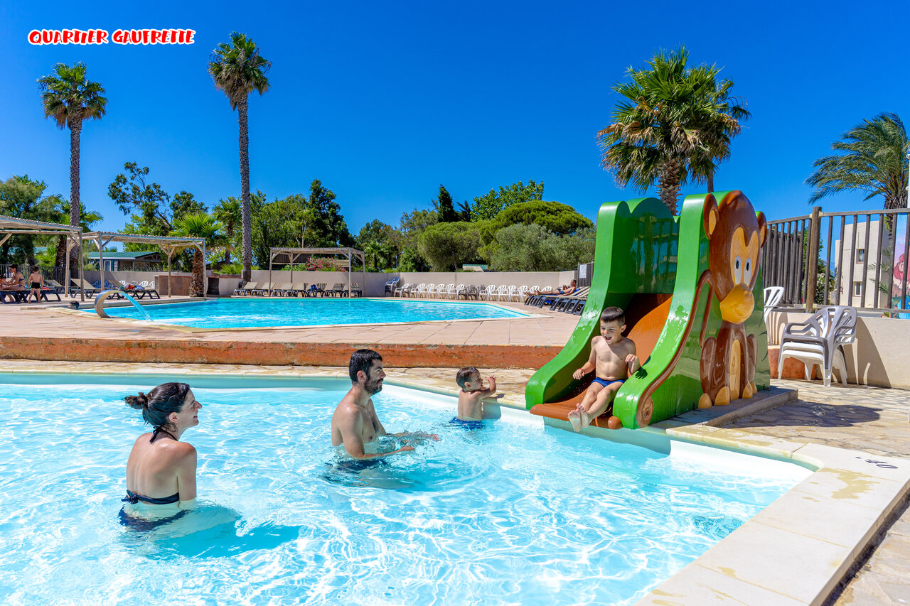 Familiezwembad met kinderwaterglijbaan en palmbomen op camping CAPFUN Las Bousigues in Le Barcar�s (66).