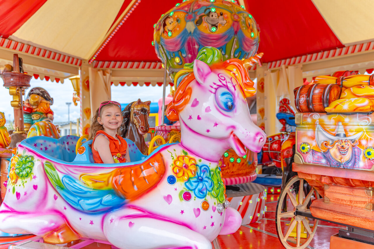 Lachend kind op een eenhoorn draaimolen op camping VAGUES OCEANES Licorne in Duinkerke (59).