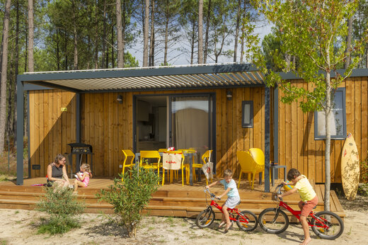 Moderne stacaravan met terras, gezin en fietsende kinderen op camping CAPFUN Lila in LINXE (40).