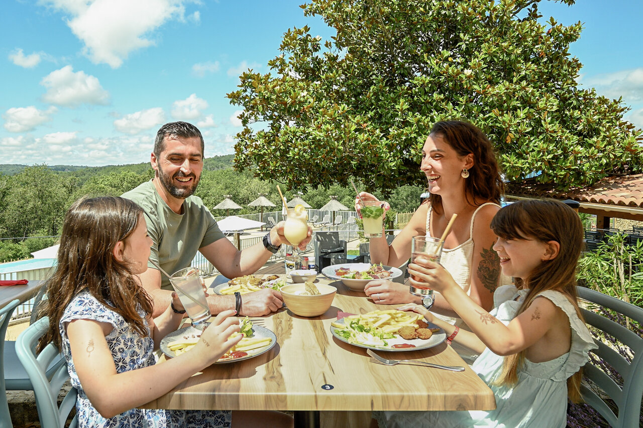 Lachende familie luncht op het terras van het restaurant-bar op camping CLICOCHIC Linotte in Le Bugue.