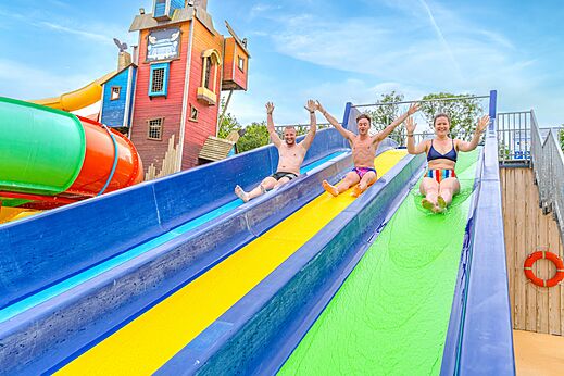 Drie personen glijden van kleurrijke waterglijbanen op camping CAPFUN Lodge in SARZEAU (56).