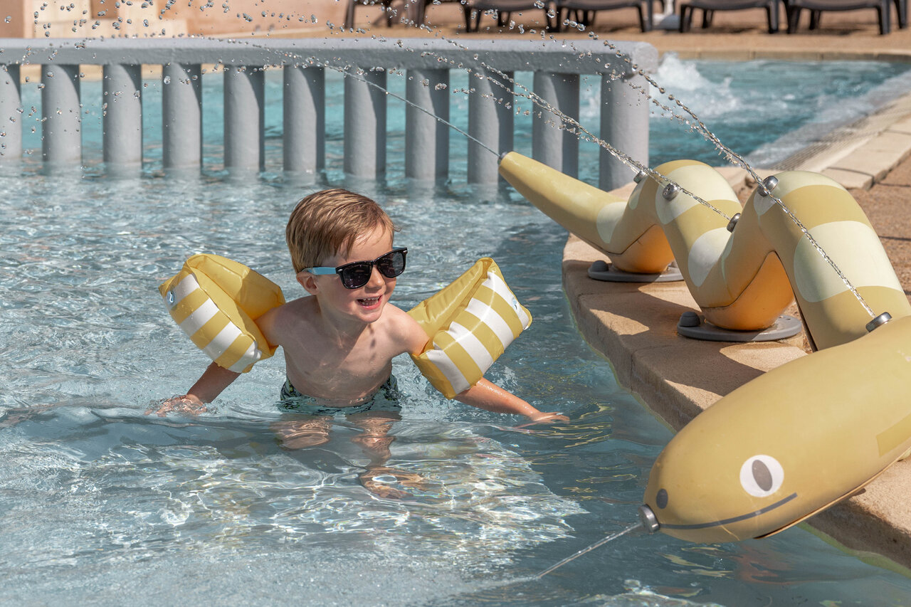 Lachend kind met zwembandjes, waterspelen zwembad camping CLICOCHIC Lou Cantaire Fayence.