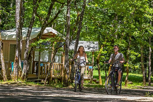 Koppel fietst op bospad op camping CLICOCHIC Lou Castel in Castelnaud-la-Chapelle.