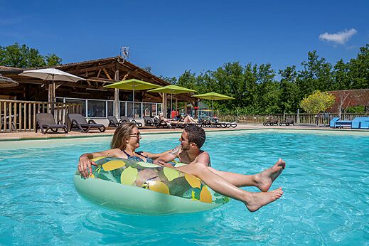Koppel ontspant op opblaasband in groot buitenzwembad op camping CLICOCHIC Lou Castel in Castelnaud-la-Chapelle (24).