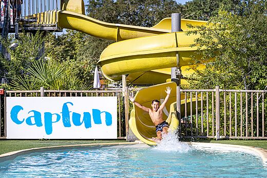 Gele waterglijbaan en kind in het zwembad op camping CAPFUN Lou Puntaou in LEON.