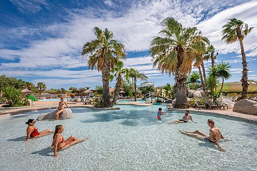 Buitenzwembad, waterglijbaan en palmbomen op camping CAPFUN Lou Village in Vendres (34).