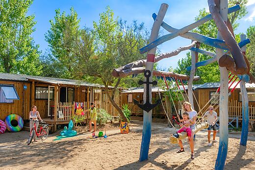 Houten speeltuin, schommel, familie en stacaravans op camping CAPFUN Lou Village.