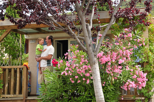 Stacaravan met bloemrijk terras en lachende familie op camping CAPFUN Malissonne in LA CADIERE D'AZUR (83).
