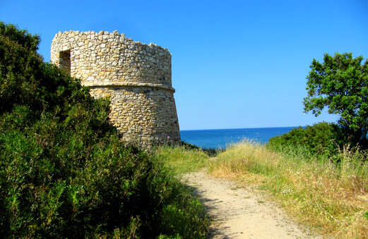 Historische stenen toren aan zee, zandpad op Corsica.