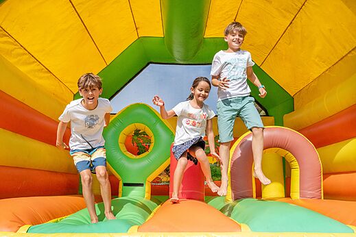 Kinderen op kleurrijke opblaasbare spelen op camping VAGUES OCEANES Marina Landes.