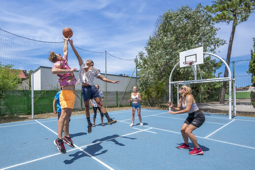 Jongeren basketballen op een multisportterrein op camping VAGUES OCEANES Marina Landes in Mimizan (40).