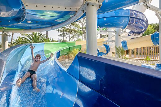 Lachende jongen glijdt van een grote blauwe waterglijbaan op camping VAGUES OCEANES Marina Landes in Mimizan (40).