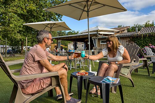 Paar proostend met cocktails aan de bar van camping CLICOCHIC Médoc Bleu in Carcans (33).