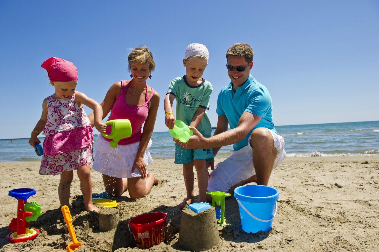 Familie bouwt zandkastelen op het strand bij camping CAPFUN Mer et Soleil in Cap d'Agde.
