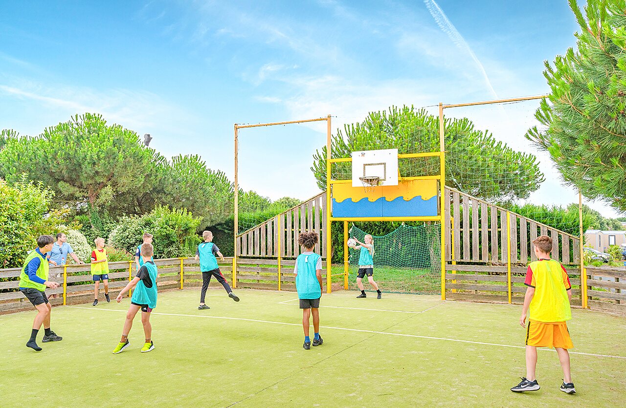 Kinderen spelen basketbal op multisportterrein op camping VAGUES OCEANES in Givrand.