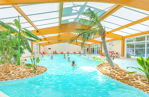 Overdekt tropisch zwembad met palmbomen en zwemmers op camping VAGUES OCEANES Micheli�re, Givrand (85).