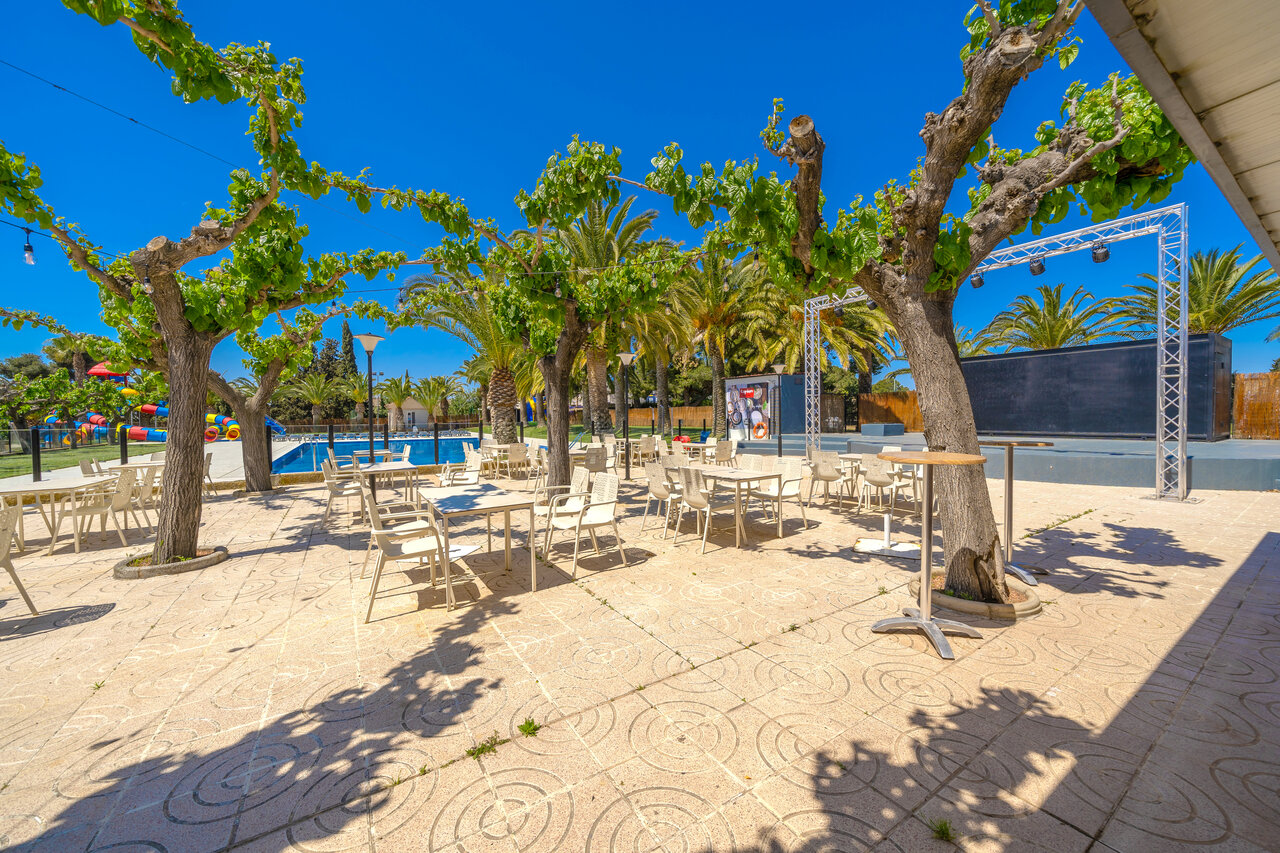 Schaduwrijk restaurantterras, zwembad en podium op camping CAPFUN Mirmanda in Cambrils.