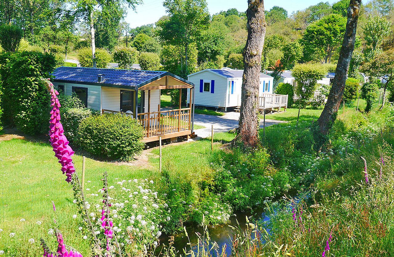 Stacaravans met houten terrassen en beekje op camping VAGUES OCEANES Moulin de Cadillac in Noyal-Muzillac (56).