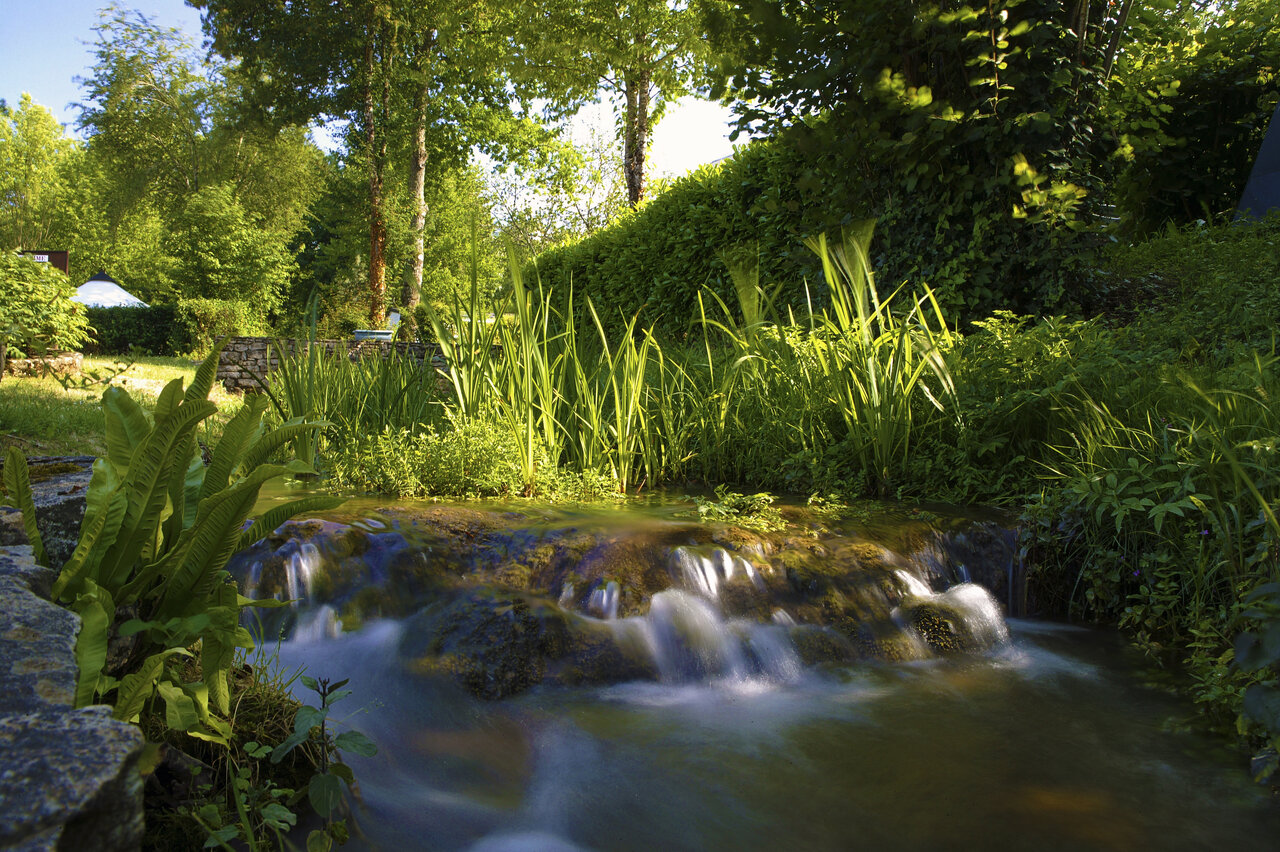 Natuurlijke waterval en weelderig groen op camping CLICOCHIC Moulin du Roch in Saint Andre D'Allas.