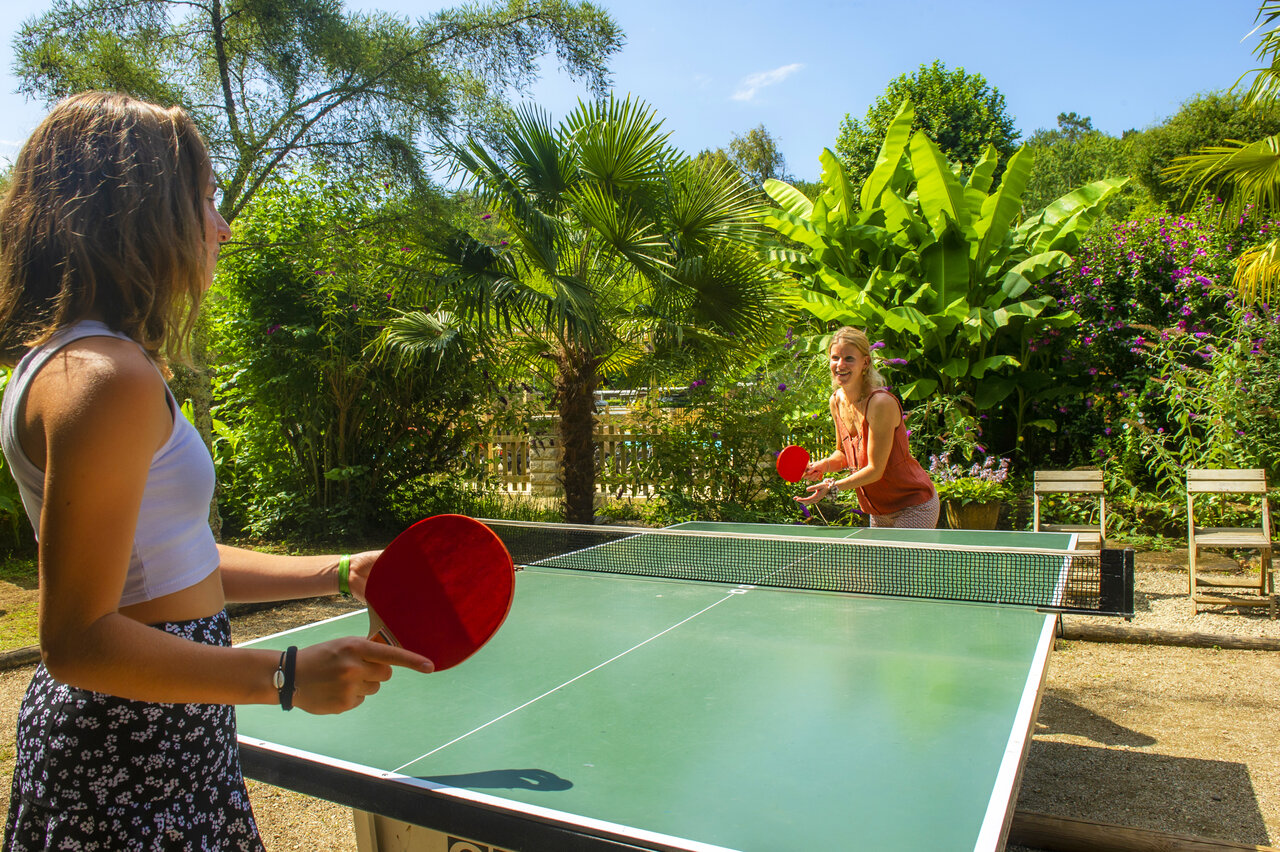 Twee vrouwen spelen tafeltennis buiten op camping CLICOCHIC Moulin du Roch.