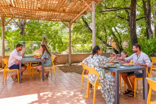 Gezinnen en koppels dineren op het schaduwrijke terras van het restaurant op camping CLICOCHIC Orée d'Azur in OPIO (06).