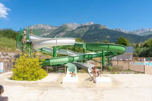 Waterglijbanen en spelende kinderen, met bergen op de achtergrond op camping CAPFUN Oursière in Villard de Lans (38).
