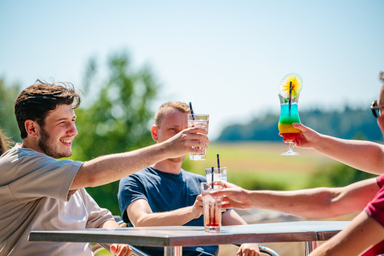Vrienden proosten met kleurrijke cocktails op terras bij camping CAPFUN Pachy in FOSSES LA VILLE.
