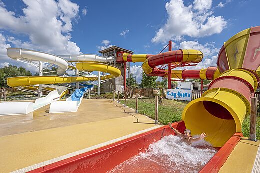 Kleurrijke waterglijbanen en kind glijdend op camping CAPFUN Paradis de Bazas in BAZAS (33).