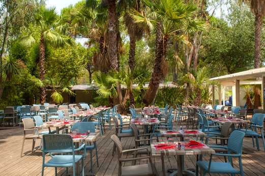 Buitenrestaurant, tafels en stoelen onder palmbomen, camping CAPFUN Parc et Plage.