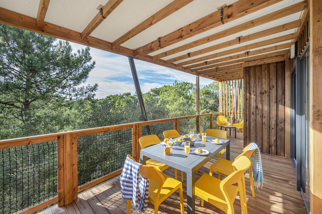 Houten terras van stacaravan met tafel en gele stoelen, boszicht op camping CLICOCHIC Petit Bec in St Hilaire de Riez (85).