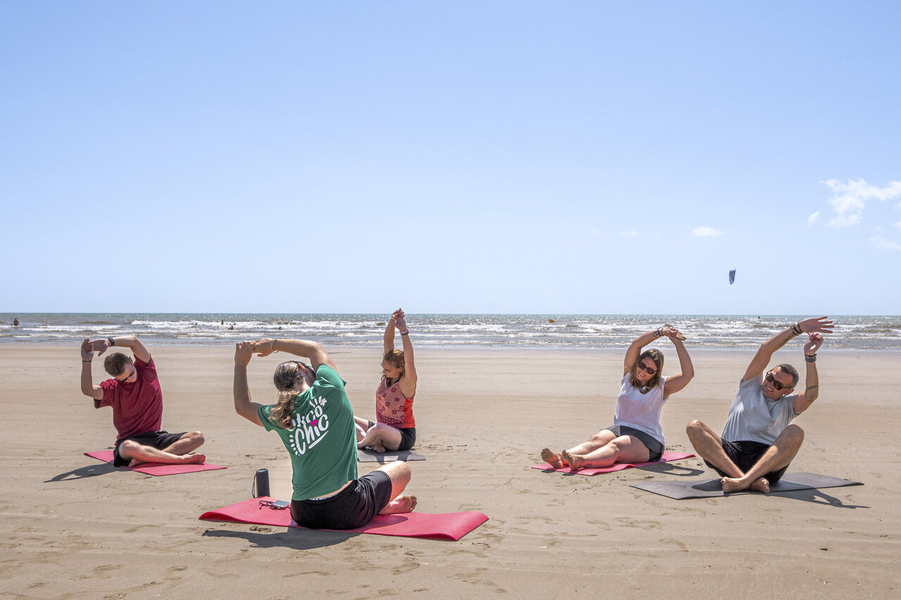 Volwassenen doen yoga op het strand bij camping CLICOCHIC Petit Bec.