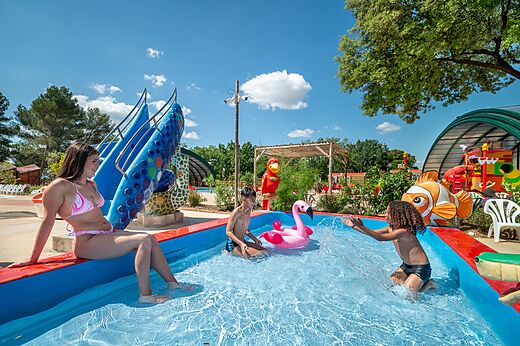 Kinderen en jonge vrouw spelen in speelzwembad met glijbaan op camping CAPFUN Pin�des du Luberon in PERTUIS (84).