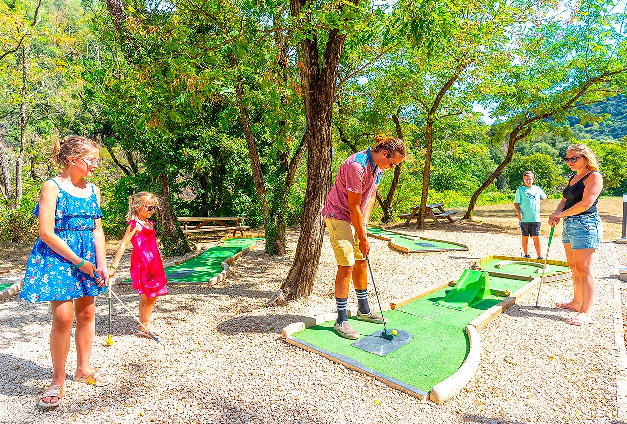 Familie speelt minigolf op schaduwrijke baan bij camping CAPFUN Plantas in SAINT VINCENT DE DURFORT (07).