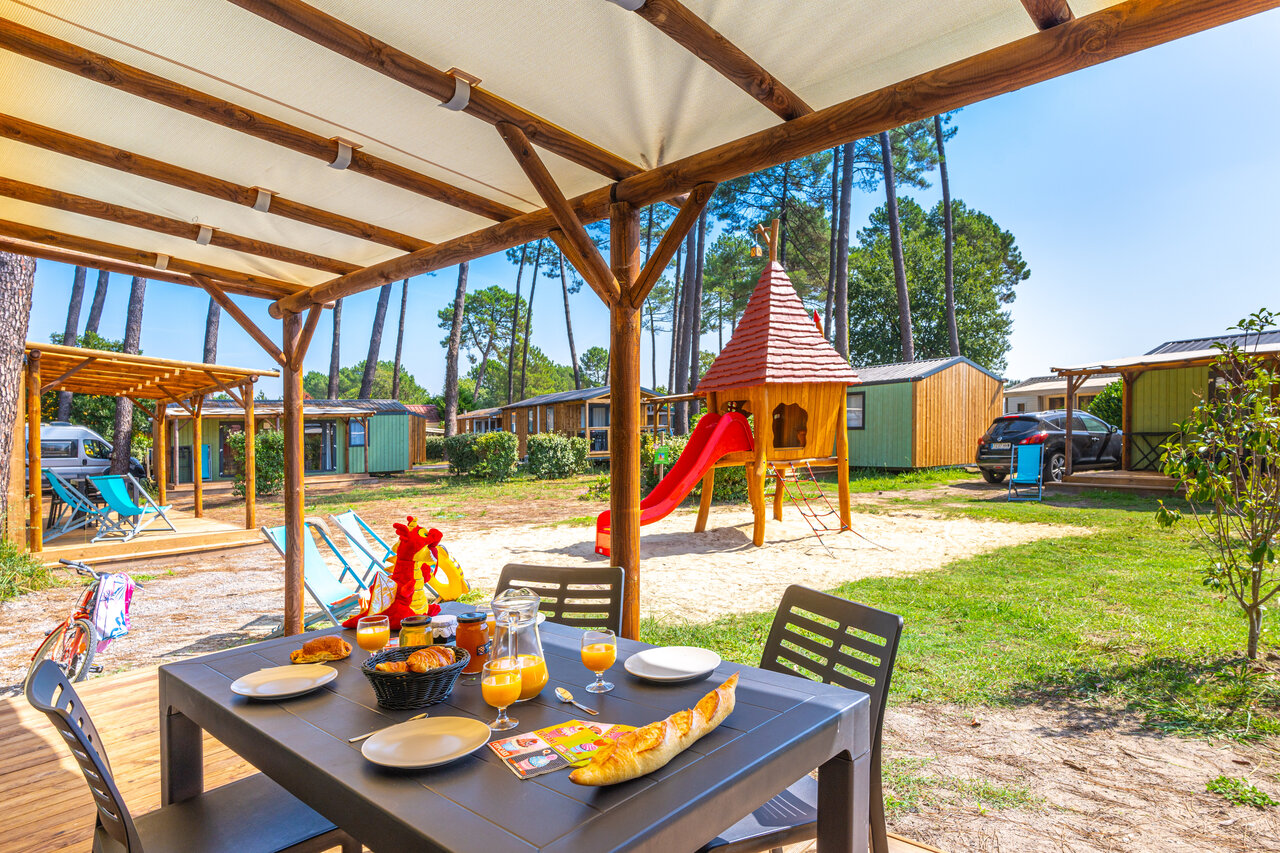 Ontbijt op Mobil-home terras met kinderspeeltuin op camping CAPFUN Pomme de Pin in Saubion (40).