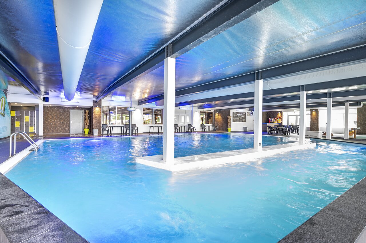 Verwarmd binnenzwembad met blauwe verlichting en ontspanningsruimte op camping CAPFUN Ponderosa in Ulicoten.