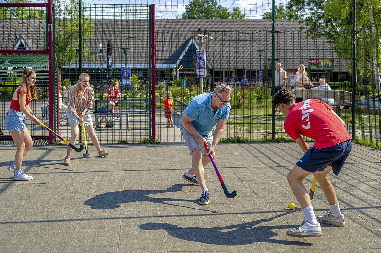 Familie speelt hockey op een multisportterrein op camping CAPFUN Ponderosa in Ulicoten.