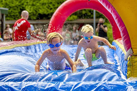 Kinderen vermaken zich op een opblaasbare waterglijbaan op camping CAPFUN Ponderosa in Ulicoten.