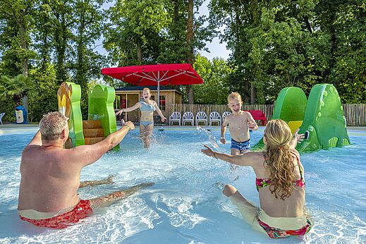Buitenzwembad met waterspeeltoestellen en gezin plezier makend op camping CAPFUN Ponderosa in Ulicoten.