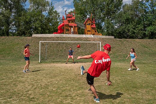 Familie voetbalt op sportveld met speeltuin op camping CAPFUN Les Portes du Beaujolais in Anse (69).