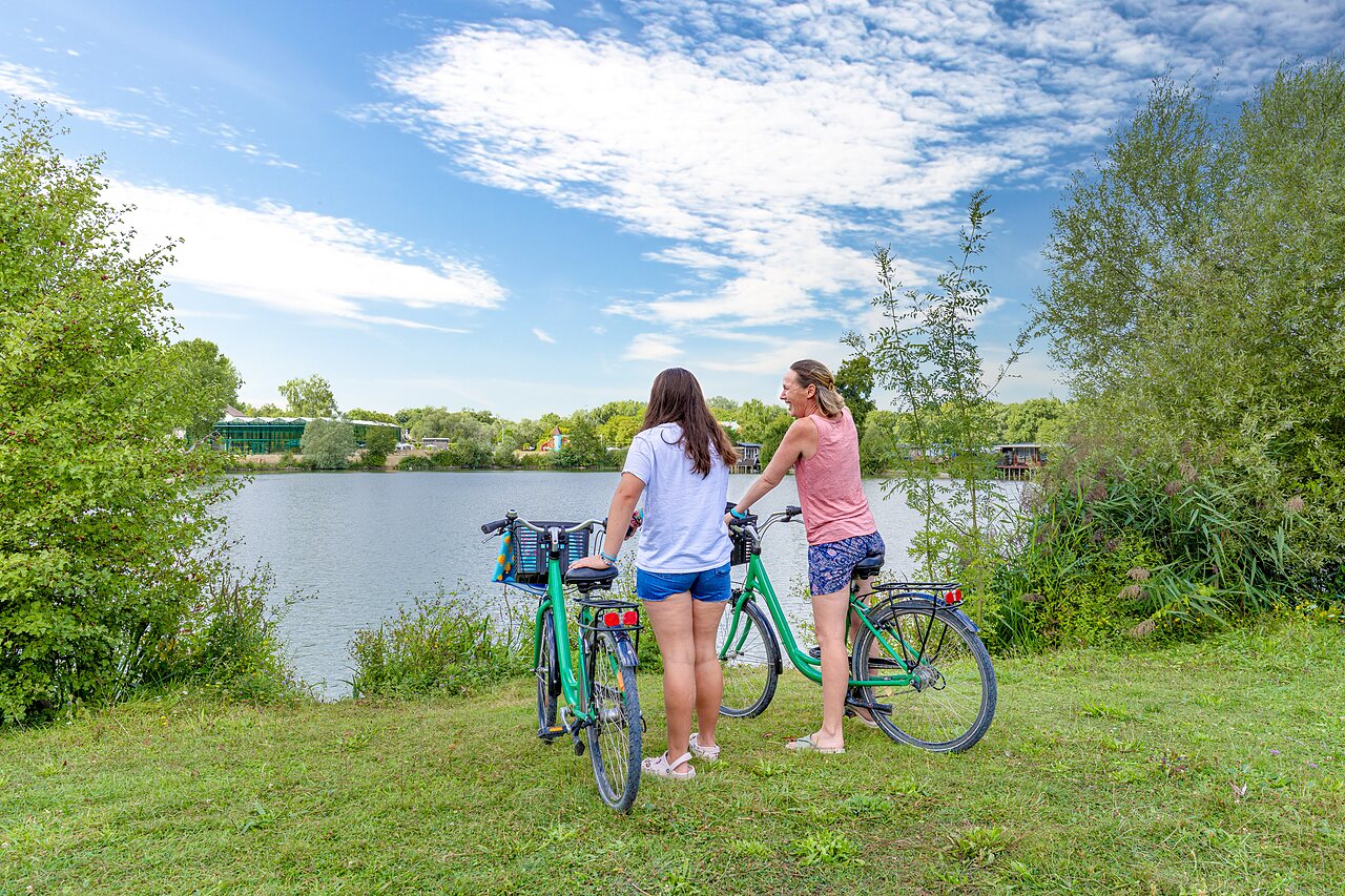 Twee vrouwen op de fiets aan het meer, groene natuur op camping VAGUES OCEANES Pr�s de la Fontaine � Gouaix (77).