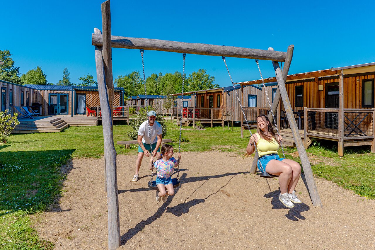 Blije familie op de schommels, Mobil-homes op de achtergrond op camping VAGUES OCEANES Pr�s de la Fontaine � Gouaix (77).