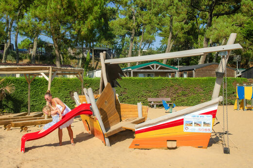 Speeltuin met houten boot, glijbaan en kinderen op camping CAPFUN Prises in La TRANCHE SUR MER (85).
