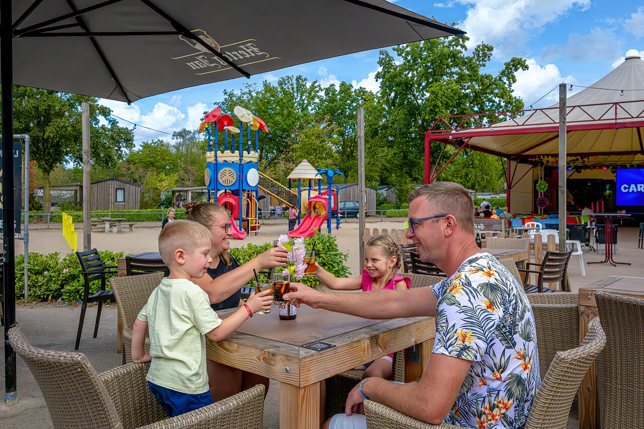 Familie proostend bij speeltuin en animatiepodium op camping CAPFUN Rakelbos in Westelbeers.