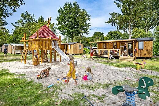 Houten speeltuin met glijbaan en kinderen op camping CAPFUN Rakelbos in Westelbeers.
