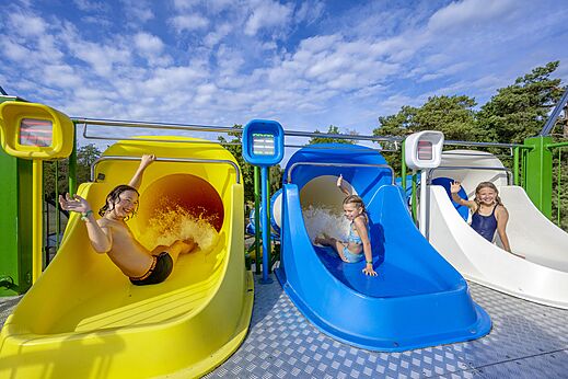 Kinderen glijden van de kleurrijke waterglijbanen op camping CAPFUN Rakelbos in Westelbeers.