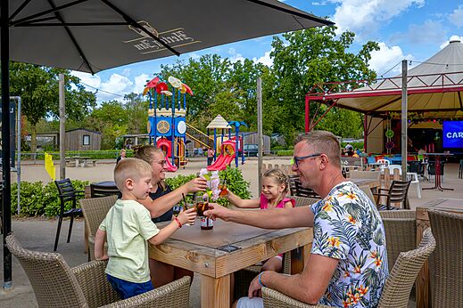 Familie genietend van bar en speeltuin op camping CAPFUN Rakelbos in Westelbeers.