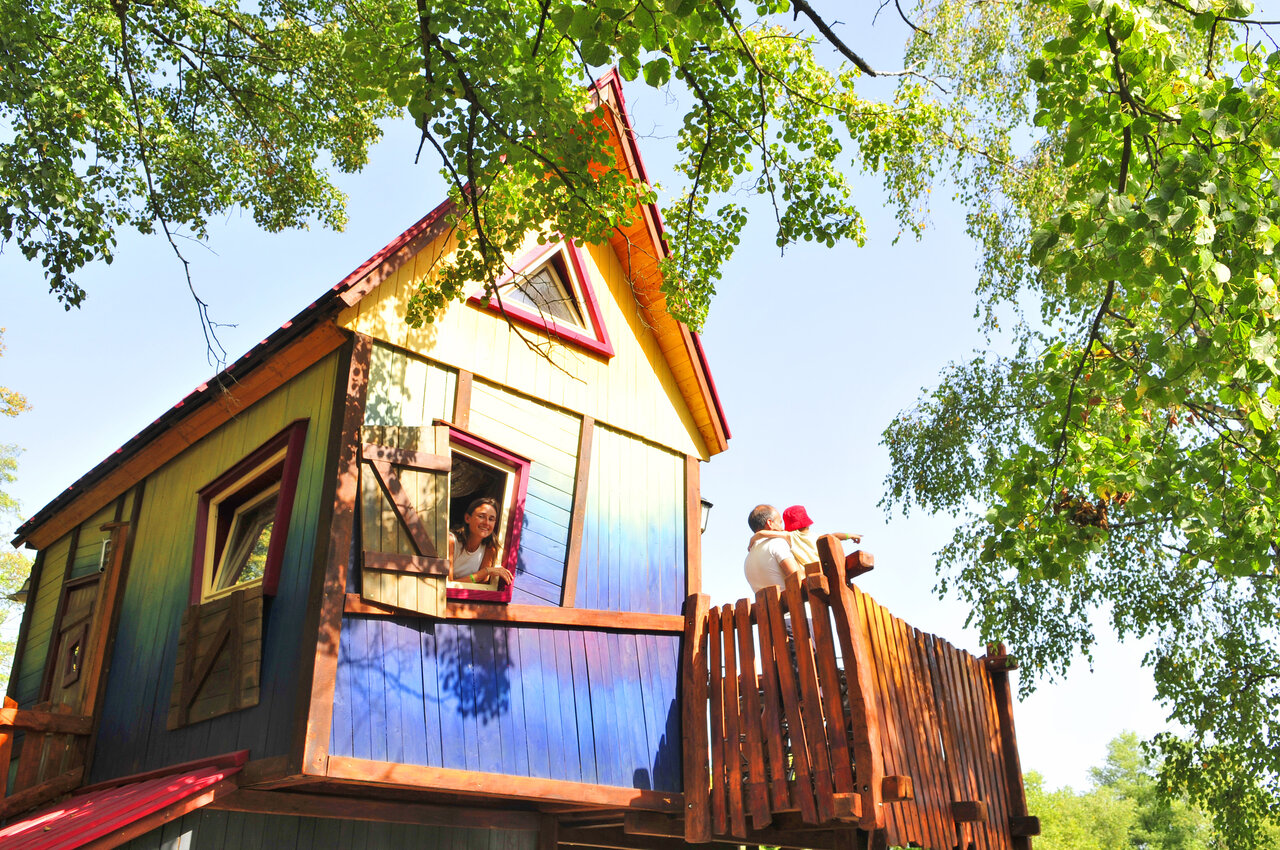 Kleurrijke boomhut met familie op balkon op camping CAPFUN R�gni�re in Villette d'Anthon.