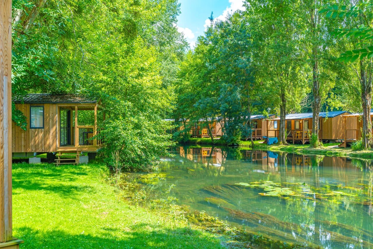 Houten Mobil-homes aan een groene rivier, weelderige natuur op camping CAPFUN La Rivi�re in Valence-en-Poitou (86).
